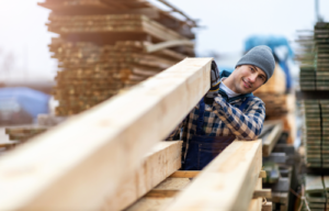 Man in timber warehouse holding and looking down the length of a timber piece